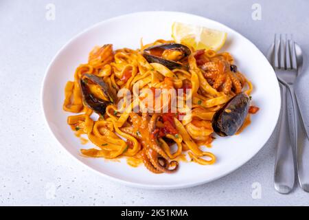 Marinara-Pasta mit Garnelen, Oktopus und Muscheln. Hausgemachte Nudeln mit Meeresfrüchten in Tomatensauce. Traditionelles italienisches Gericht. Selektiver Fokus, Nahaufnahme. Stockfoto