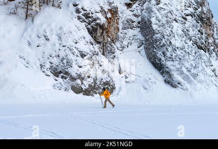 Seitenansicht der jungen Frau in gelber Kleidung mit Rucksack Skifahren in der Nähe von Felsen und Klippen aktiv gesunder Lebensstil Wintersport Wandern Stockfoto