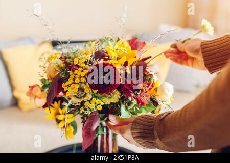 Nahaufnahme der Blumenarrangements. Frau macht Herbst Strauß von Sonnenblumen Dahlien Rosen und Zinnien in Vase zu Hause. Einrichtung im Innen- und Herbststil in Gelb Stockfoto