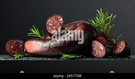 Spanischer Blutwurst oder Blutwurst mit Rosmarin auf schwarzem Hintergrund. Stockfoto