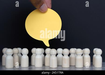 Gruppe von Holzpuppen und leere Sprechblase auf schwarzem Hintergrund. Stockfoto