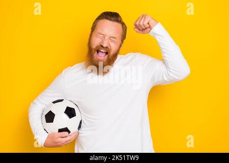 Porträt der erfreut überglücklich Mann halten Fußball heben Faust Schrei ja isoliert auf gelbem Hintergrund Stockfoto