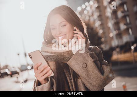 Foto von ziemlich positive Mädchen halten verwenden Telefon Hand berühren drahtlose Kopfhörer genießen Spaziergang draußen Stockfoto