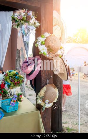 Strohhüte, die mit Blumen am Schaufenster verziert sind. Wunderschöne handgefertigte Produkte. Produkte, Kleinunternehmen Stockfoto