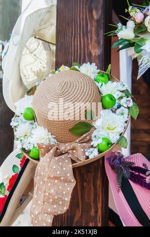 Strohhüte, die mit Blumen am Schaufenster verziert sind. Wunderschöne handgefertigte Produkte. Produkte, Kleinunternehmen Stockfoto