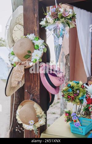 Strohhüte, die mit Blumen am Schaufenster verziert sind. Wunderschöne handgefertigte Produkte. Produkte, Kleinunternehmen Stockfoto