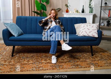 Reife Frau trinkt Rotwein und sitzt auf dem Sofa Stockfoto