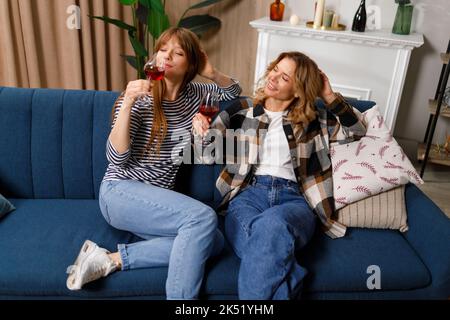 Mutter und junge Tochter unterhalten sich freundlich und trinken Wein, während sie auf dem Sofa im Wohnzimmer sitzen Stockfoto