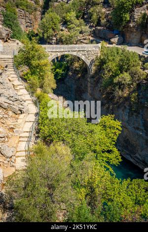 Alte Bogenbrücke über die Koprucay-Schlucht im Koprulu-Nationalpark in der Türkei. Panoramablick auf die Schlucht und den blau stürmischen Berg Stockfoto