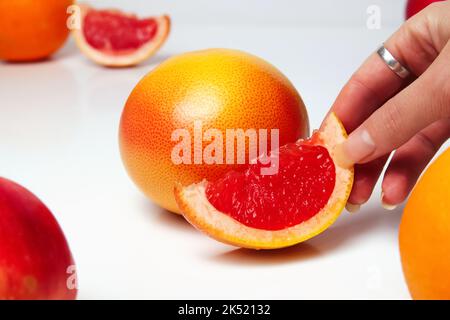 Unschärfe-Effekt der weiblichen Hand, die ein Stück einer roten Grapefruit auf weißem Hintergrund hält. Gesundes Lebensmittelkonzept. Frischer Orangensaft. Veganes, vegetarisches Konzept. Banner Stockfoto