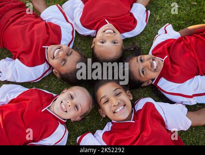 Fröhliche Fußballkinder entspannen sich auf dem Feldsportportrait für Gruppenzusammenarbeit, Teamarbeit und Motivation. Fußballmädchen Kinder Gesicht auf dem Boden liegen Stockfoto