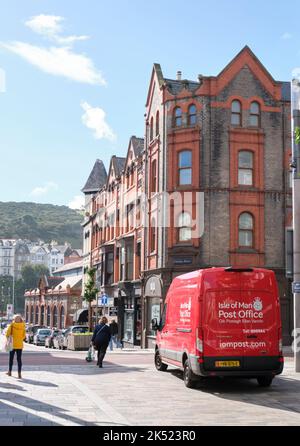 Ein charakteristisches rotes Postauto im Stadtzentrum von Douglas, eine Menscheninsel mit viktorianischen Gebäuden und Passanten in der Ferne. Stockfoto