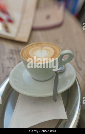 Eine Tasse Cappuccino mit einem Milchschaumherz auf einem silbernen Tablett Stockfoto