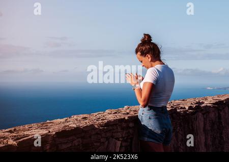 Digitale Nomadin, die am Telefon arbeitet, während sie an einem Aussichtspunkt zum Meer ist Stockfoto
