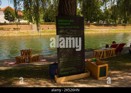 Ljubljana, Slowenien - September 4. 2022. Ein Informationsschild in slowenischer Sprache eine Bibliothek im Freien am Ufer des Flusses Ljubljanici Stockfoto