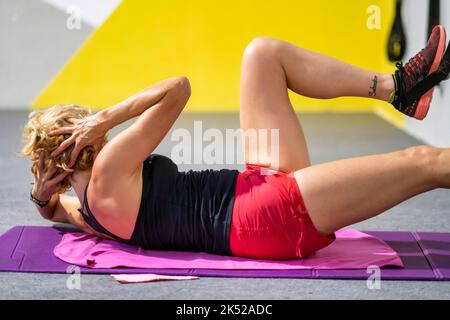 Echte junge reife kaukasische Frau in einer Sportkleidung in einem Fitnessstudio tun knirscht auf einer Matte. Fitnesskonzept. Stockfoto