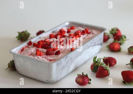 Hausgemachtes Erdbeereis, das aus dem Gefrierschrank in einer Brotdose mit Erdbeerscheiben serviert wird. Drei Zutaten Eis aus frischen stra Stockfoto