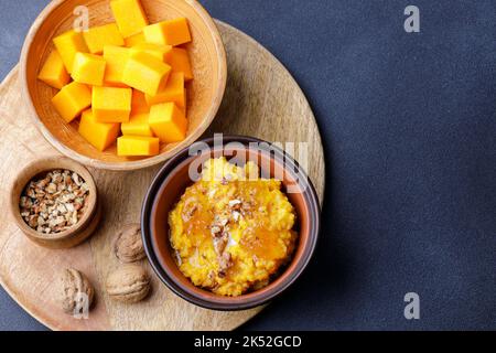 Süßer Kürbisbrei in Tonschüssel mit Marmelade und Nüssen und rohen Kürbiswürfeln Stockfoto