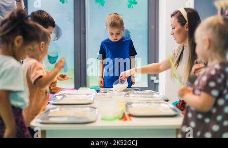 Kinder und Lehrer stehen um den Tisch und machen sich bereit zu malen, Kindergarten. Hochwertige Fotos Stockfoto