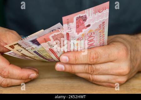 Der Mann hinter dem Schreibtisch hat eine Garbe paraguayischen Geldes in der Hand Stockfoto