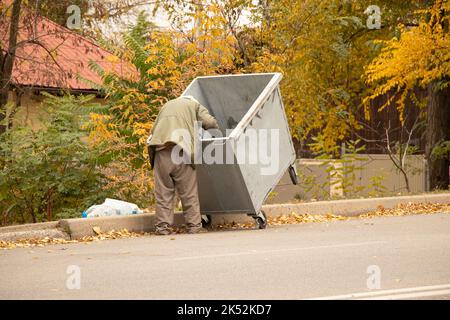 Schmutziger obdachloser Mann, der nach Essen im Mülleimer sucht, obdachloser Mann und Müllabfuhr, auf der Suche nach Nahrung, wandernder Mann Stockfoto