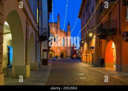 Enge gepflasterte Straße zwischen alten historischen Gebäuden, die mit Weihnachtslichtern in Alba, Italien, beleuchtet sind. Stockfoto