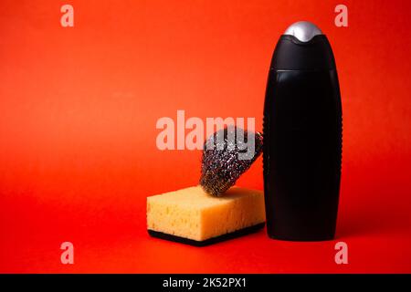 Reinigungsmittel in einer schwarzen Flasche und Schwämme auf rotem Hintergrund. Stockfoto