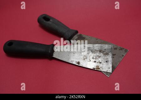 Kitt-Messer mit Holzgriffen, Closeup ein neues metallisches Kitt-Messer isoliert auf weißem Hintergrund. Einzelmesser mit schwarz rotem Gummigriff Stockfoto