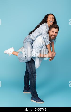 Lachender junger europäischer Mann, der die Frau aus dem Nahen Osten zurückhält, Spaß zusammen hat, Freizeit genießt Stockfoto