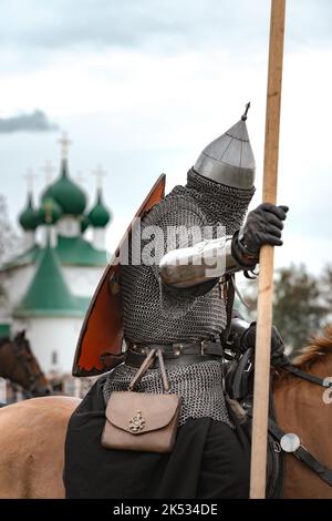 Reiter in Kettenpanzerung, Helm und Schild auf einer Robe auf Pferd auf dem Hintergrund eines bewölkten Kirchentages Stockfoto