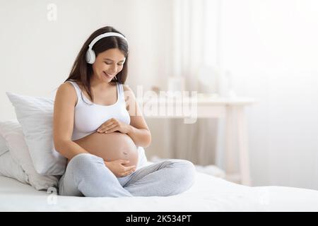 Glücklich lächelnde junge, schwanger Frau, die Musik in Kopfhörern hört Stockfoto