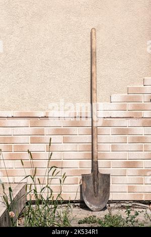 Alte, schmutzige Schaufel gegen die Fliesenwand am Sommertag Stockfoto