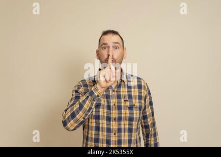 Ernst gut aussehende Männchen, hält den Vorderfinger auf den Lippen, versucht Verschwörung zu halten, schaut beiseite, sagt: Shh, bitte schweigt. Einzelaufnahme von Stockfoto