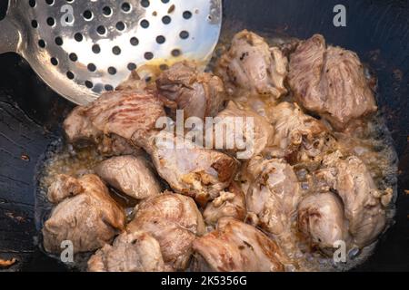 Große Stücke von Lamm Schafe in Öl gebraten mit Blasen in einem schwarzen Kessel Nahaufnahme Kochen Lebensmittel Stockfoto