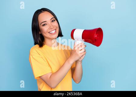 Foto-Porträt von atemberaubenden jungen Dame japanischen halten Megaphon toothy Lächeln tragen trendige gelbe Kleidungsstück auf blauem Hintergrund isoliert Stockfoto