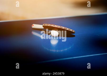 Holzschläger für Tischtennis und weiße Kugel auf der blauen Tabelle liegen. Tischtennis Paddel Ausrüstung. Hobby, Aktivität. Stockfoto