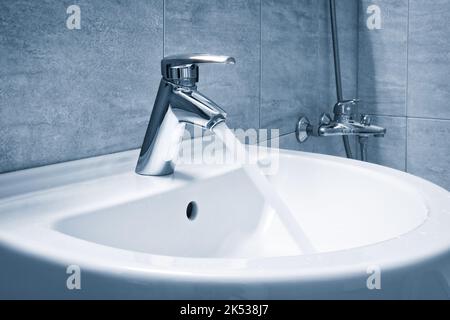 Wassermischer im Bad. Wasserhahn aus Chrom-Material, Wasserhahn mit Wasser in Blauton Stockfoto