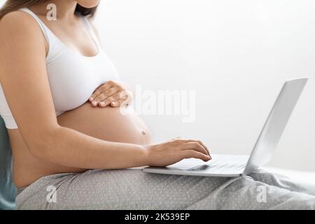 Schwanger Frau mit Laptop-Computer, sitzt auf dem Bett zu Hause Stockfoto