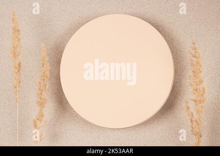 Runde beige Plattform Podium Stand und trocken gebogene Pflanze auf weißem Sand Hintergrund. Minimale kreative Komposition Hintergrund für Kosmetika oder Produkte Stockfoto