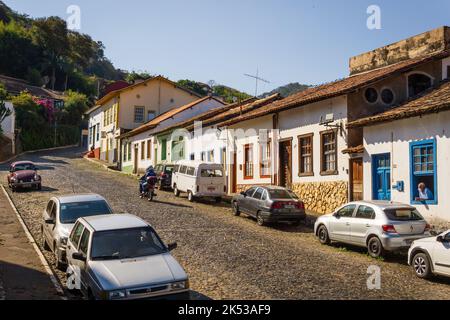 Kopfsteinpflasterstraße mit kolonialen Gebäuden und einem Mann, der aus dem Fenster in Sabará, Minas Gerais, Brasilien, blickt. Stockfoto