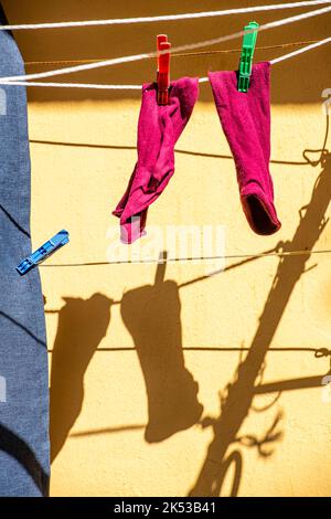 Ein Paar rosa Socken an einer Wäscheleine trocknen im Sonnenschein von Türen aus. Wäschetag, Wäschewaschen, Wäscheklammern, am Wäscheleinen befestigt. Stockfoto