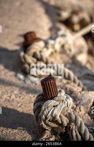 Abstrakte Seile und Schiffspoller aus rostigen alten Stahlnadeln auf der Hafenseite. Knüpfseile und Liegefäden in einem Yachthafen für Boote Stockfoto