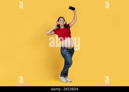 Happy Young Schwangeren Frau Mit Smartphone Musik Hören In Kopfhörer Und Tanzen Stockfoto