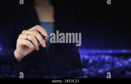 Geschäftsfrau halten Stift auf virtuellen Bildschirm, dunkler Hintergrund, Nahaufnahme. Nahaufnahme der Hand, die einen schwarzen Marker hält, um etwas zu schreiben. Stockfoto