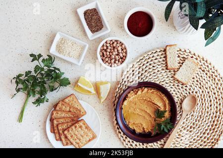 Hausgemachte vegetarische Vorspeise. Traditioneller Hummus mit Getreideplätzchen, Petersilie, Zitronenscheiben. Petersilie, Paprika, römische Kümmel, Kichererbsen, Sesam in Stockfoto
