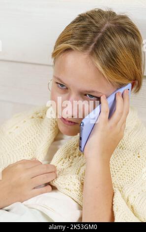 Teen Mädchen sitzt auf dem Bett und emotional Gespräche am Telefon. Vertikaler Rahmen. Nahaufnahme. Stockfoto