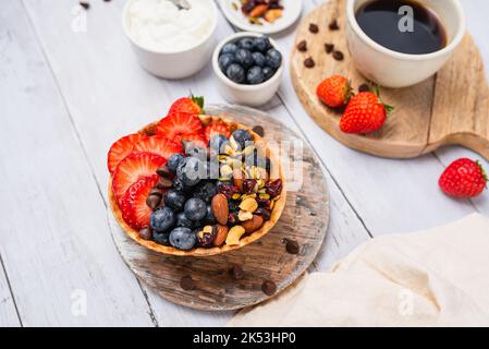 Joghurt und Obst in einer Waffelschale. Griechischer Joghurt in Eiswaffelschüssel mit Obst und Nüssen, gesundes, ernährungsfreundliches Dessert. Fruchtige Waffelschale. Stockfoto