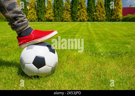 Ein Fußballball und ein Kinderbein am Sonnentag im Hintergrund eines Hinterhofs Stockfoto