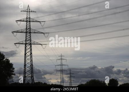 Die dunklen Silhouetten der elektrischen Festnetzleitungen in Deutschland, Europa. Dunkle Wolken symbolisieren den Wandel in der Elektrik und Energieversorgungskette in der Welt. Stockfoto