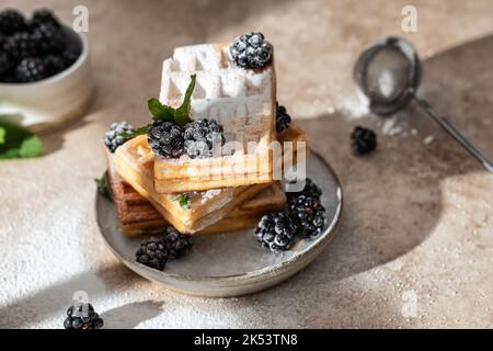 Stapel von hausgemachten belgischen Waffeln aus nächster Nähe mit Brombeere und Puderzucker auf dem Küchentisch. Konzept für das Frühstück am Morgen Stockfoto